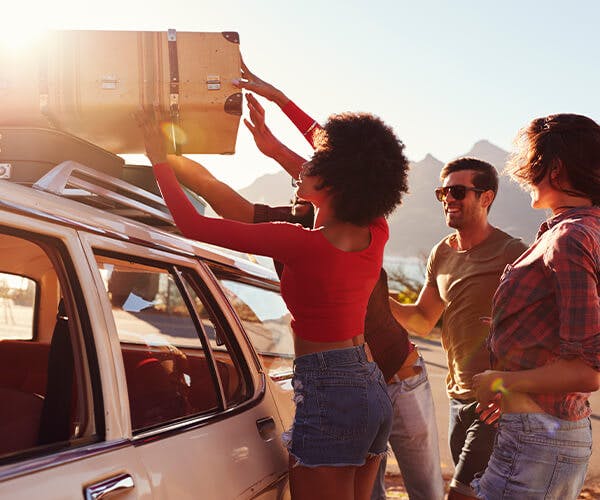 Friends loading a suitcase on a vehicle