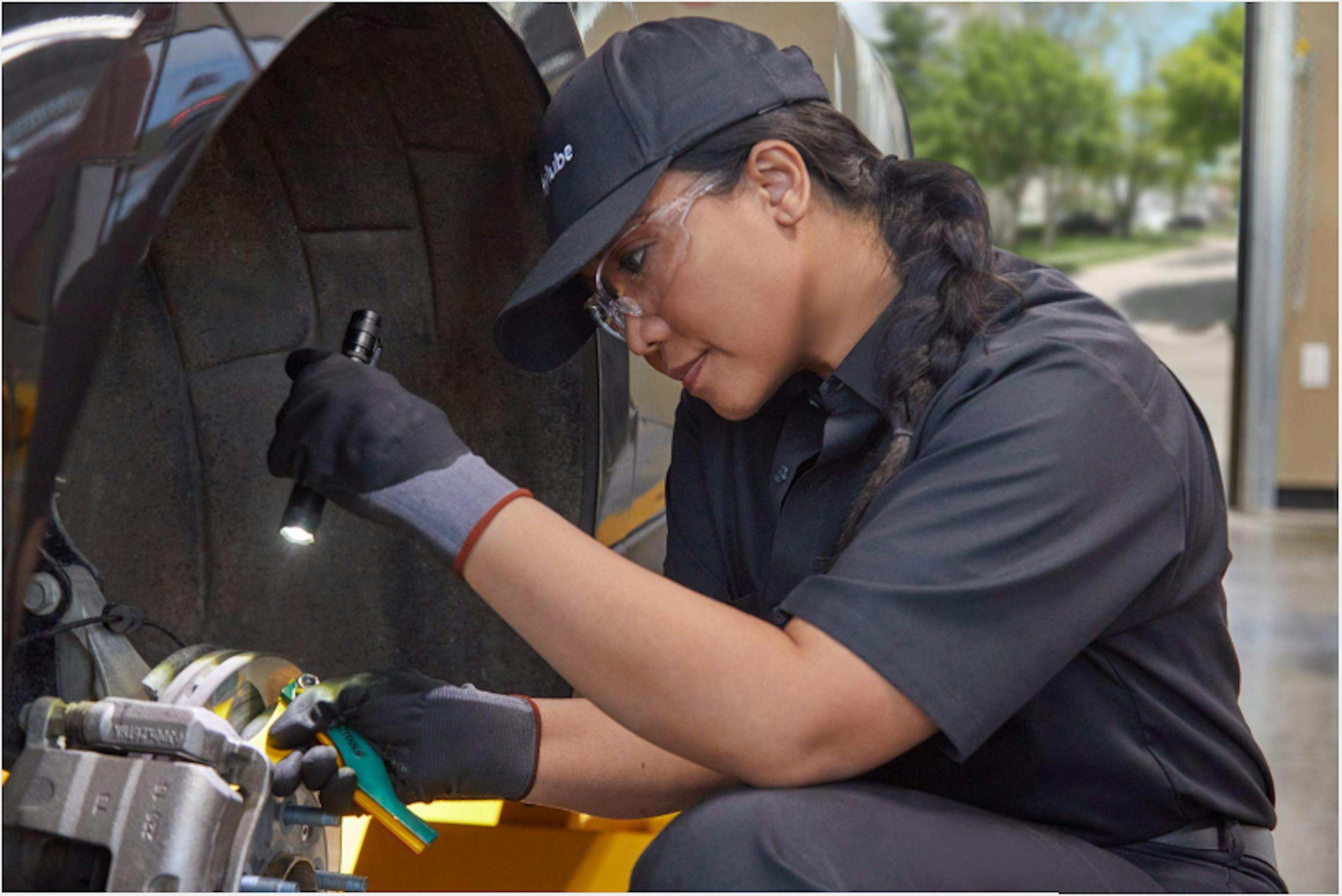 A Jiffy Lube service member using a flashlight to check the remaining life in a cars brake pad