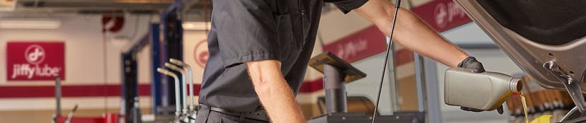 Jiffy Lube service member adding motor oil to a vehicle during an oil change and fluid top off