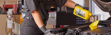 Jiffy Lube service member adding Pennzoil motor oil to a vehicle during an oil change and fluid top off