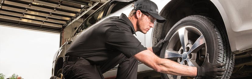 Jiffy Lube technician wearing all black uniform replacing a tire after balancing the wheel