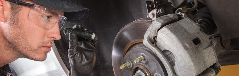 A Jiffy Lube technician inspecting a vehicle brake rotor & brakes pads with small flashlight