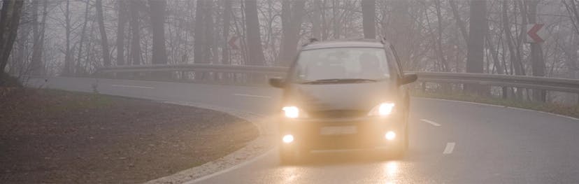 Halogen headlight of a sedan vehicle shining through light misting rain